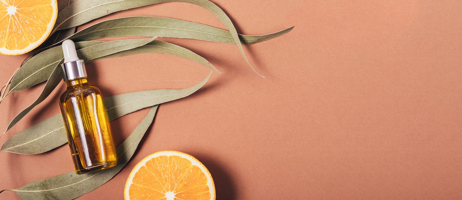 Flacon d'huile naturelle entouré de feuilles d'eucalyptus et d'oranges